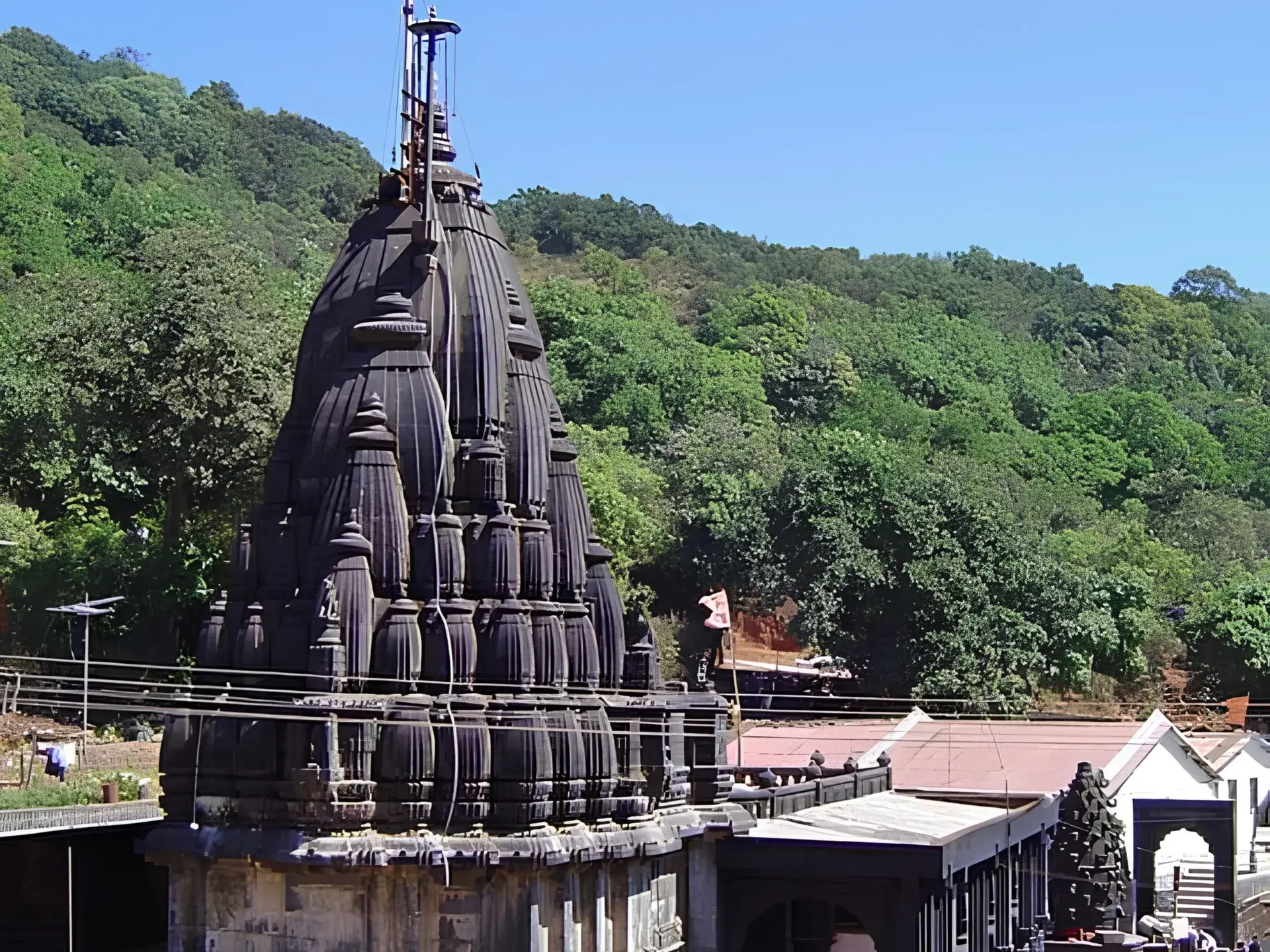 Dark stone shikhara of Bhimashankar Jyotirlinga temple against forested Sahyadri hills under a clear blue sky